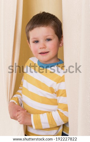 The boy with the white-and-yellow striped shirt peeking from behind the curtains