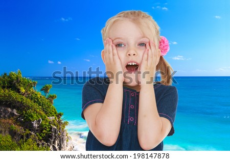 Surprised small blonde girl standing against the blue of the sea
