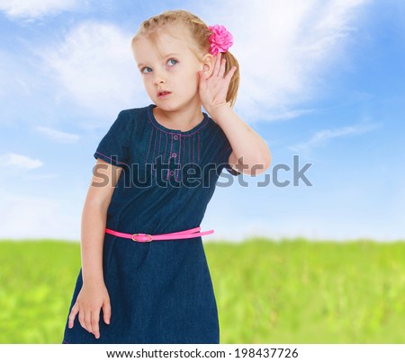 girl put her hand to his ear and listens to the sounds of nature that sound from a nearby field.