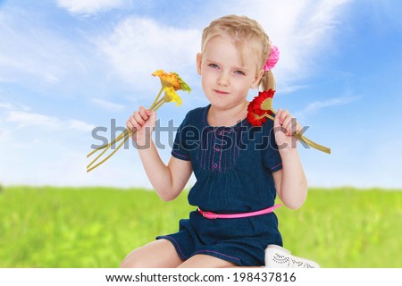 girl holding colorful flowers sitting on her knees in good weather on a background of bright green summer morning.