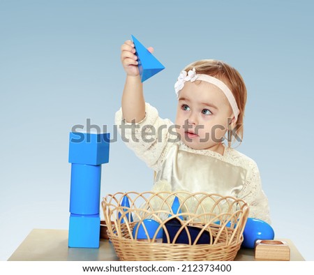 little girl sitting at the table playing with cubes and pyramids on a blue background in the Montessori classroom.the concept of a happy childhood, education of children, teens