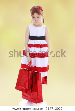 Girl in a striped dress holding red paper shopping bags.The concept of development of the child younger years.