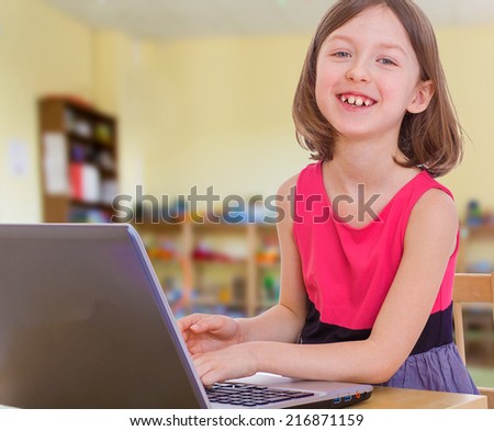 Pretty girl laughing pressing the buttons on the laptop.Concept of childhood and family values.