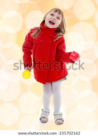 Charming little girl in a red coat with plastic toys in the hands Happiness, winter holidays, new year, and childhood.