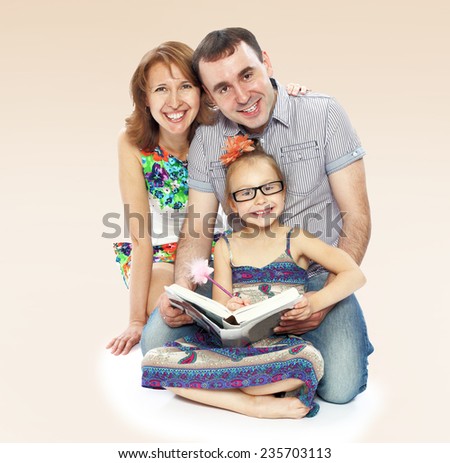 Happy young family mom dad and little daughter reading a book sitting on the floor.