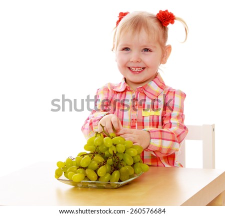 laughing blond little girl eating grapes sitting at the table - isolated on white.