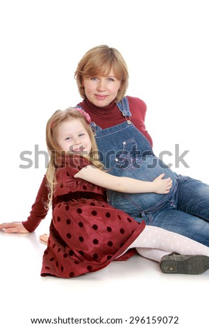 Happy little blonde girl in a long brown dress with polka dots hand stroking the belly of his beloved pregnant mom - isolated on white background