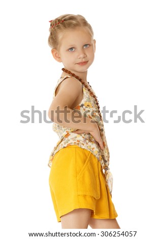 Stylish fashion blond girl in a long trendy necklace.The girl is dressed in a colorful silk blouse with short sleeves and yellow short shorts. A girl stands sideways turning to the camera with a