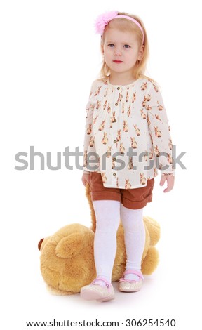 Beautiful little blonde girl pulls on the floor Teddy bear holding one of his paws. The girl is wearing a white shirt and brown shorts-Isolated on white background