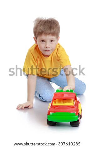 Fair-haired little boy with brown eyes sitting on the floor and rolls plastic machine-Isolated on white background