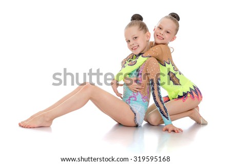 Pretty girls gymnasts dressed in sports suits sat down on the floor . Girls hugging and smiling at camera-Isolated on white background