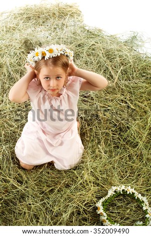 Cute little girl plays in the village on the haystack. She tries on a head a wreath of field daisies . Top view - Isolated on white background