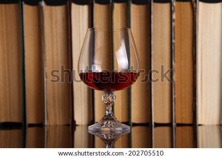Glass of brandy on a reflective surface with books