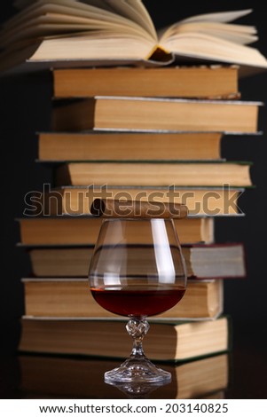Glass of brandy on a reflective surface with books and cigar
