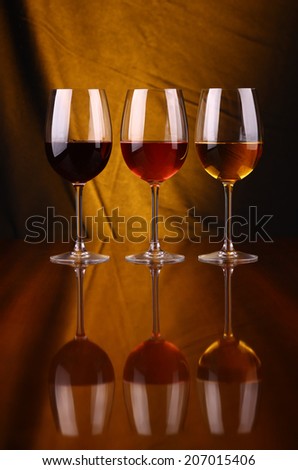 Glasses of red, rose and white wine over a draped background lit yellow