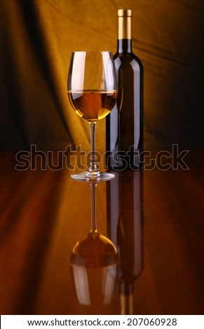 Glass and bottle of white wine over a draped background lit yellow