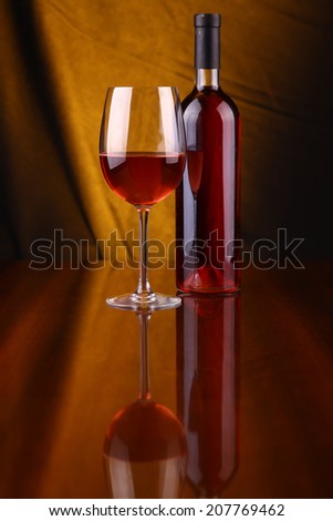 Glass and bottle of rose wine over a draped background lit yellow