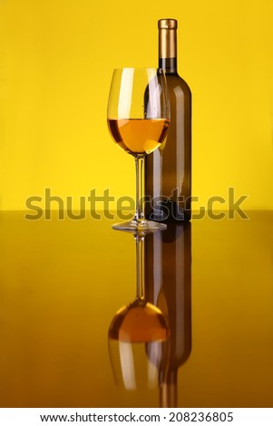 Glass and bottle of white wine over a yellow background