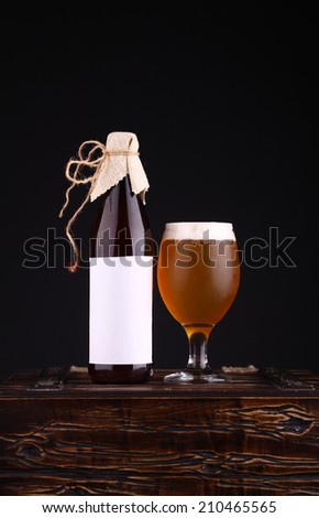 Bottle with blank label template and glass of home brewed craft beer standing on a wooden chest