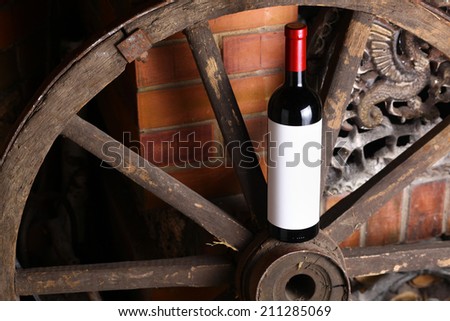 Bottle of red wine with blank label standing on an old wooden wheel near a fireplace