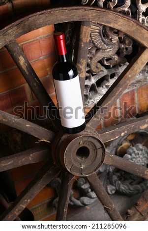 Bottle of red wine with blank label standing on an old wooden wheel near a fireplace