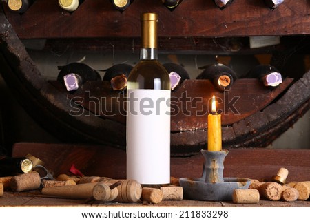 Bottle of white wine with blank label in wine cellar with used corks, bottle shelves and a burning candle
