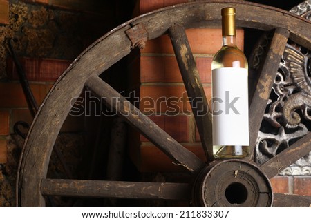 Bottle of white wine with blank label standing on an old wooden wheel near a fireplace