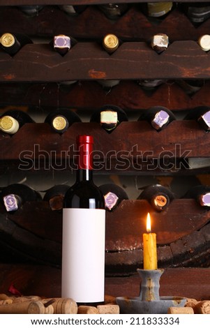 Bottle of red wine with blank label in wine cellar with used corks, bottle shelves and a burning candle