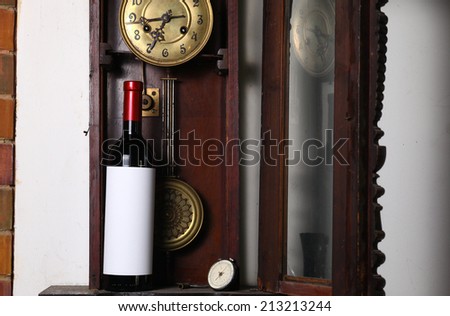 Bottle of red wine with blank label template standing inside an old clock