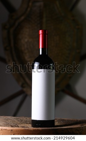 Bottle of red wine with blank label template standing on a wooden stool with an iron shield in the background