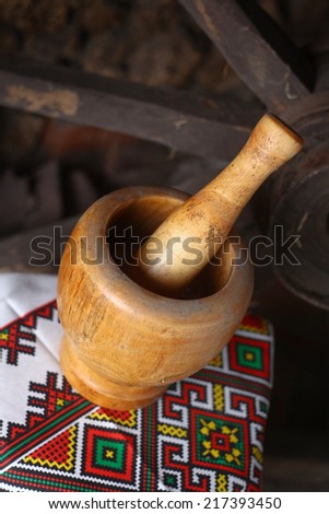 Traditional Moldovan wooden mortar and pestle standing on a traditional patterned towel with a wooden wheel in the background