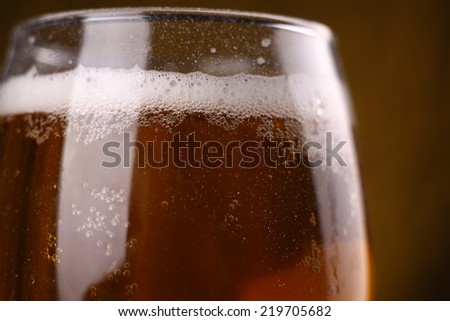 Closeup shot of a glass filled with sparkling light beer with froth over a warm lit background