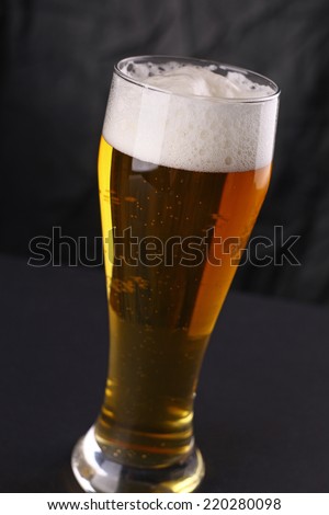 Tall glass of light beer over a gray lit background