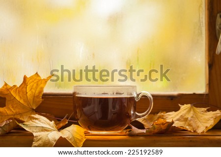 Mug of tea standing on windowsill with autumn leaves and a fogged window in the background