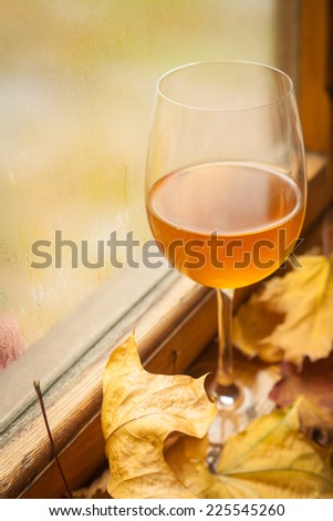 Glass of white wine standing on windowsill with autumn leaves and a fogged window in the background