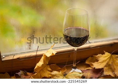 Glass of red wine standing on windowsill with autumn leaves and a fogged window in the background