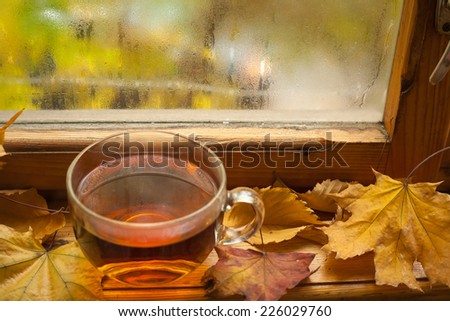 Mug of tea standing on windowsill with autumn leaves and a fogged window in the background