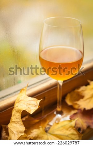 Glass of white wine standing on windowsill with autumn leaves and a fogged window in the background