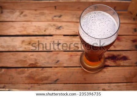 Tall glass of amber beer standing in an old dirty wooden crate