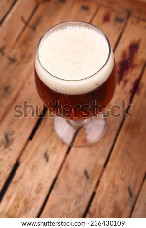Glass of amber colored beer with white foam standing in an old dirty wooden crate