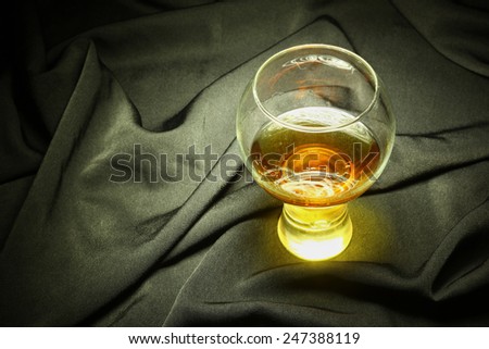 Glass of brandy standing on black crumpled fabric with light brush accent on the drink