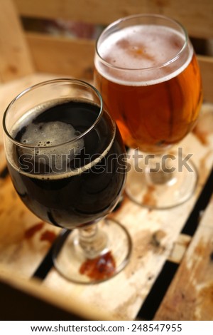 Full glass of light and dark beer standing in a dirty wooden crate
