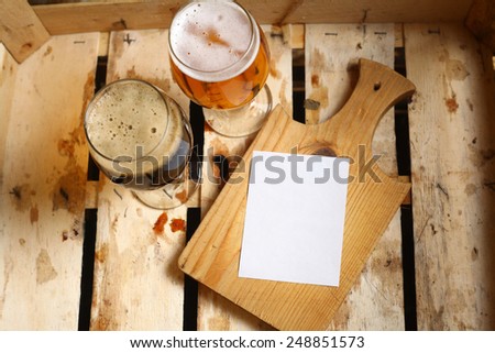 Empty note sheet on a wooden cutting board with full beer glass in a wooden crate
