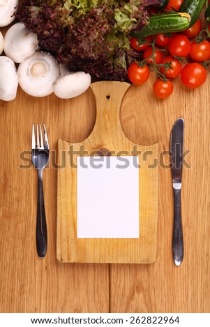 Empty note sheet on a cutting board with knife and fork and vegetables nearby