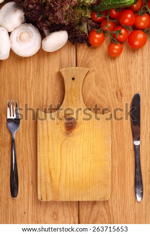 Knife and fork near a wooden cutting board with vegetables nearby