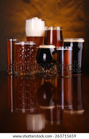 An assortment of various beer glass shapes and styles on a wooden table with a drapery in the background