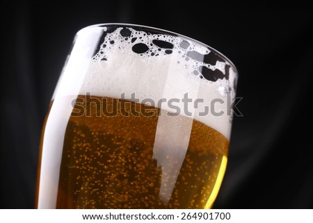 Tall glass of sparkling lager beer over a dark background