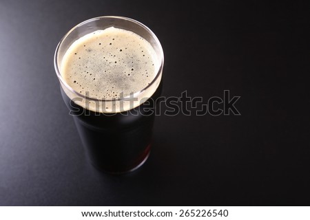 Nonic pint glass full of dark stout ale over a dark background