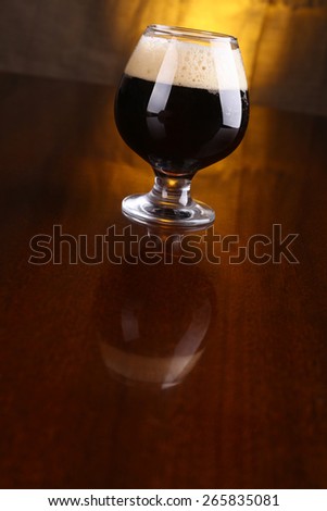 Snifter glass with black stout beer on a wooden table with a warm colored drapery in the background