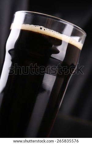 Nonic pint glass full of dark stout ale over a dark background